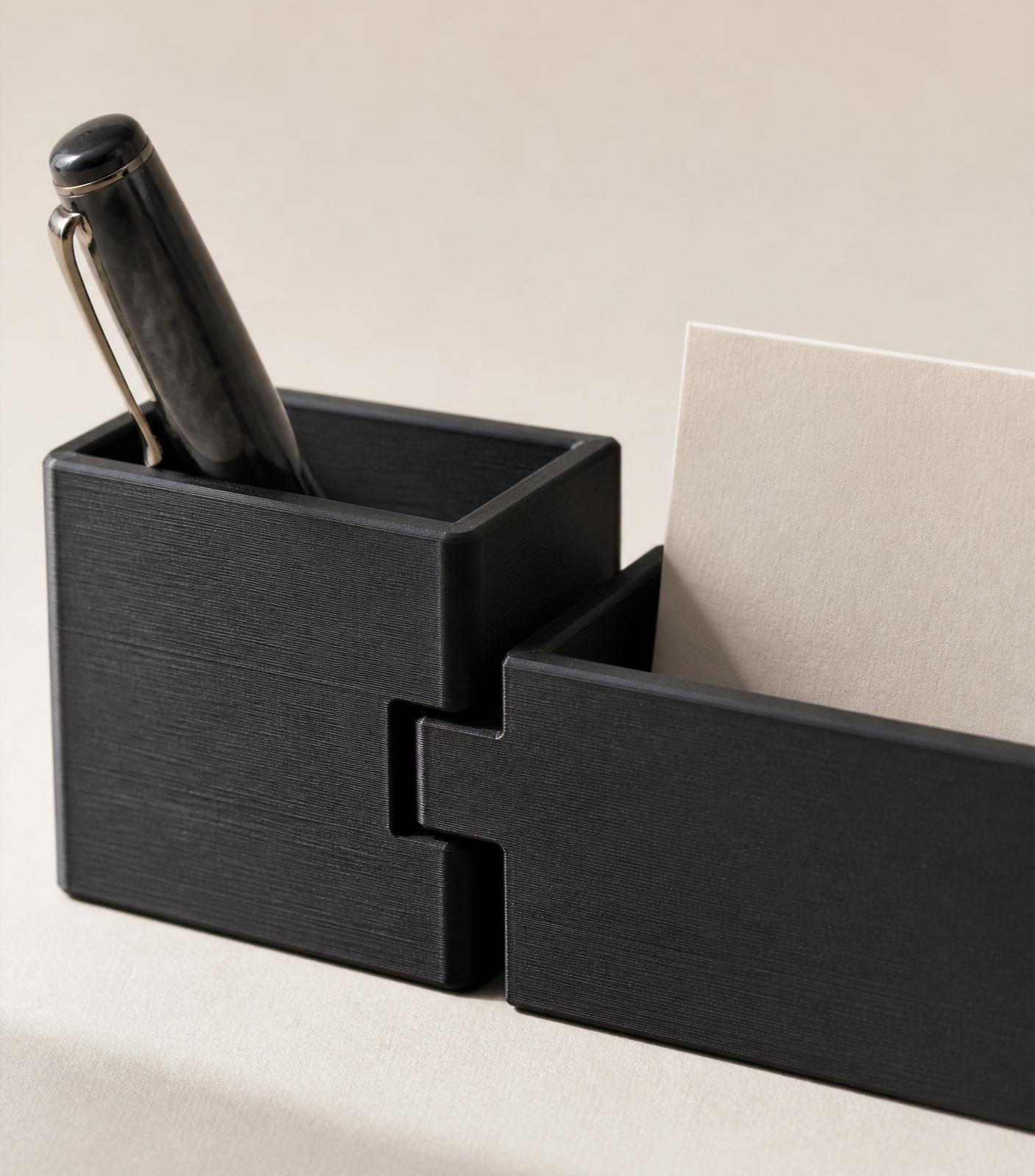 Detail of two charcoal black modular pieces connecting via a tab-and-slot joint, holding a fountain pen and a folded card